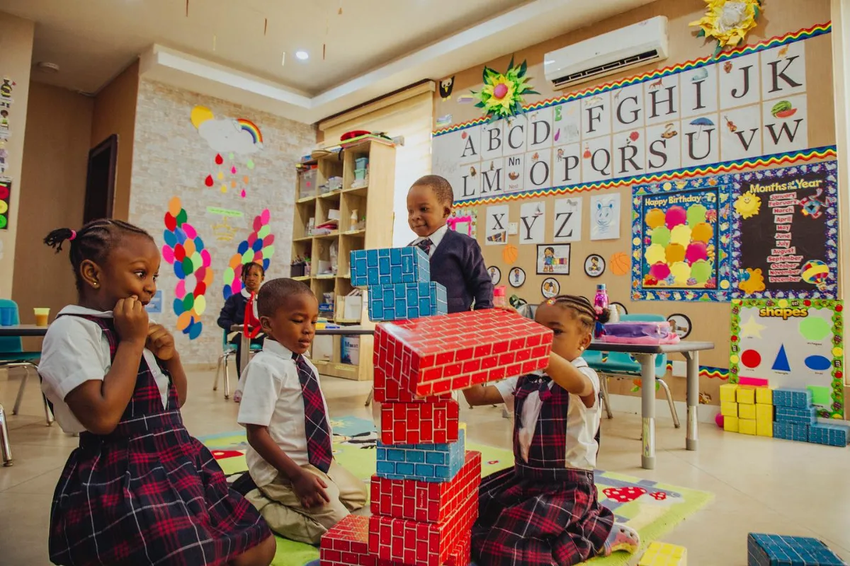 Young children building a tower with large blocks in a classroom.