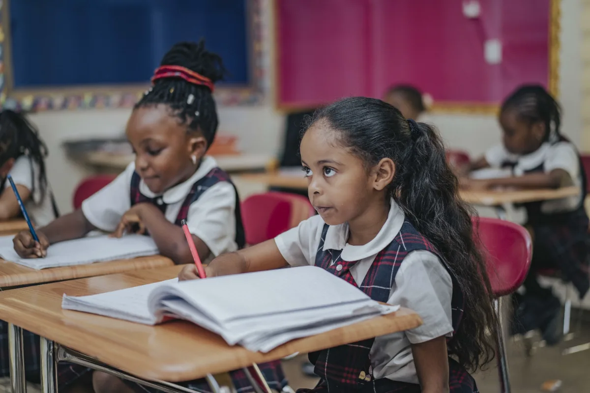 Students writing in their notebooks at classroom desks.