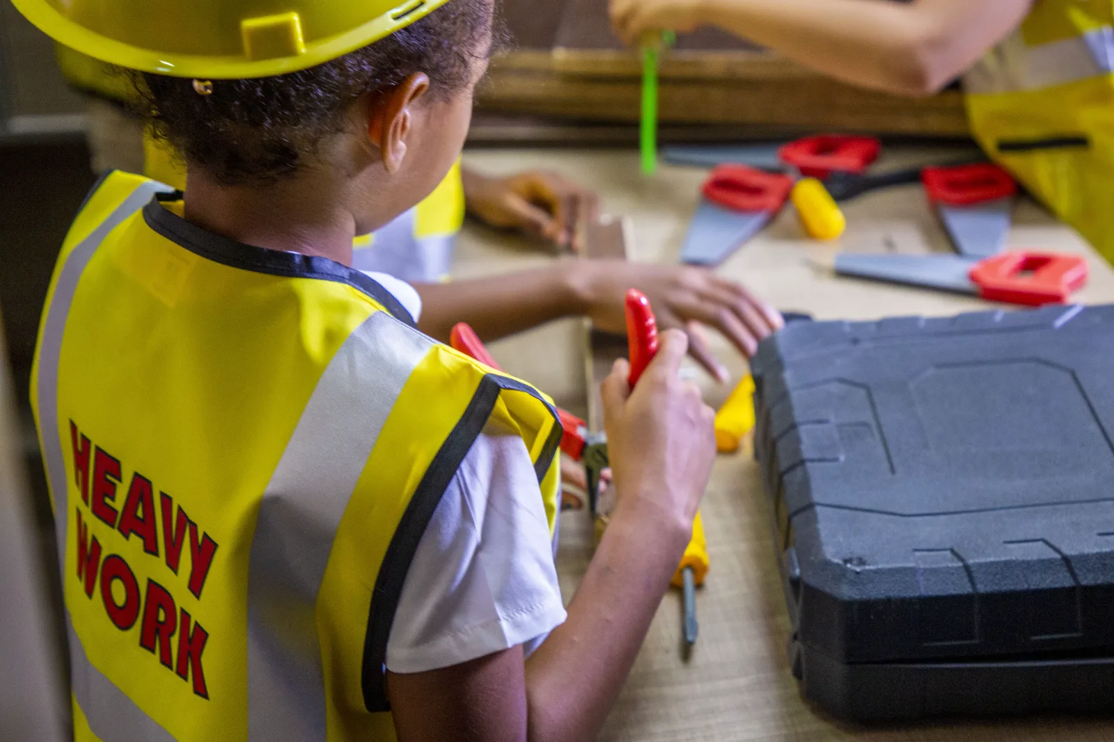 A student in a work vest using toy tools with a classmate.
